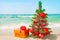 Christmas tree and golden gift with big red bow on the sea beach