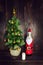 Christmas tree with golden toys, fireless candle, bottle of champagne in Santa Claus costume on wooden background