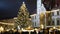 Christmas tree luminous and shines beautiful decorated with golden ornaments and flasks, historical architectural city