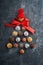 Christmas tree made of chocolate truffles, hazelnuts, anise stars, decorations, spoons and powdered sugar snow on dark background.