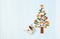 Christmas tree made of Xmas gingerbread cookies, cinnamons, cranberries and handmade furoshiki gift on blue background
