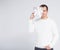 Christmas or Valentine`s day concept - man in white warm sweater covering face with gift box and posing over gray background with