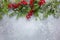 Christmas or winter background with a border of green and frosted evergreen branches and red berries on a grey vintage board. Flat