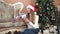 Christmas Woman dressed white sweater Santa hat sitting on floor near Christmas tree using smartphone