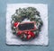 Christmas wreath with green fir branches and red framed sign and Santa hat in snow on blue background, top view with chalkboard