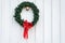 Christmas wreath made of artificial evergreen boughs and a light string, with red bow and cow bell, on a white wall