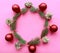 Christmas wreath of spruce branches, red baubles and pinecones on pink background.