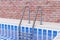 Chrome Swimming Pool Ladder in Swimming Pool in Front of Brick Wall Interior. 3d Rendering
