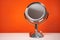 Chromed steel round magnifying mirror on handle set up on the white table. Bright orange background, single object.