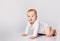 Chubby ginger little one in bodysuit, barefoot. He is sitting on floor isolated on white studio background. Close up, copy space
