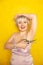 Chubby girl in dress with unshaven hairy armpits and scissors in hand on yellow background in Studio