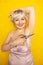 Chubby girl in dress with unshaven hairy armpits and scissors in hand on yellow background in Studio