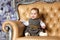 Chubby little cute baby girl sitting in a beige chair and smiling against a white Christmas tree in New year