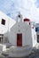 Church building in Mykonos, Greece. Chapel with bell tower and red dome. White church architecture on cloudy sky. Summer