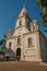 Church facade and belfry in front of a small cobblestone square with evergreen garden, in a sunny day at SÃ£o Manuel.