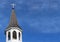 Church roof with metal cross on top and white bell tower with fluffy clouds