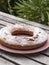 Ciambellone sprinkled with velvety sugar on ceramic plate decorated with pink cotton. Plate resting on wooden table. Outdoor veget