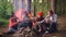 Cinemagraph loop - multiethnic group of friends girls and guys are sitting in forest around fire with drinks clinking