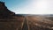 Cinematic aerial drone shot of breathtaking desert wilderness with massive rocky mountain and cars on highway in USA.