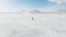 Cinematic aerial view of backpacker walking on frozen lake with beautiful winter mountains scenery background.