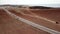 Cinematic footage - Car crossing red desert land throwing sand and dirt in the air surrounded by sea.