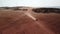 Cinematic footage - Car crossing red desert land throwing sand and dirt in the air surrounded by sea.