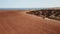 Cinematic footage - car crossing red desert land throwing sand and dirt in the air surrounded by sea.