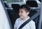 Cinematic portrait boy siting in safety car seat looking out with smiling face,Child sitting in the back passenger seat with a