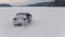Cinematic shot of grey station wagon car driving on a snowy lake.