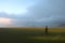 Cinematic and surreal image of a person walking through green meadows at sunset with blue mountains in the background,