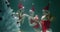 Cinematic underwater shot of young beautiful women in red hats, swimsuits exchange gifts at Christmas tree slow motion.