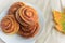 Cinnamon rolls or buns with sugar sprinkle topping on white plate and autumn leaf on table