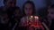 In the circle of a large family, a girl extinguishes candles on her sixth birthday.