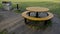 a circle-shaped camping bench with a table around it. yellow. barbecue