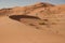 Circle-shaped dune with undulating sand and sand traces in the background large dune with horizontal lines. Oman