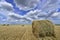 Circular haystack in windmill farm field with white grey clouds on blue sky