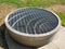 Circular metal barbeque grill on cement near grass