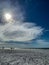 Cirrus clouds surround the sun on a windy beach day in Fort Myers, FL, while people fish in the Gulf.