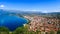 City buildings with red roofs at the shore of a lake with mountains in the background. View of Pogradec city and Ohrid lake,