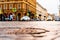 City central square after rain, car traveling on the street and pedestrians cross the road.