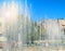 City fountain with water jets and random people, view through splashes on Sunny summer day