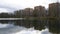 City landscape. Forest and houses around lake. Ripples on water. Stormy weather. Stormy clouds. Sky, sunlight and trees reflecting