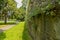 City park with a path among trees next to the medieval city wall with dandelion plants among the bricks