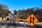 City road by a park under construction with four lanes reduced to two with in focus signs in foreground and blurred buildings an