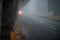 City street with cars in the distance is in poor visibility. Heavy fog on the road in the early morning. The bright light of the