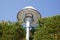 City street lamp urban lighting in day with green tree foliage