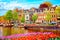 Cityscape view of the canal of Amsterdam in summer with a blue sky and traditional old houses. Colorful spring tulips flowerbed on