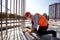 Civil engineer dressed in shirt, orange work vest and helmet measures the hole with a tape measure on the building site