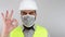 Civil engineer wearing work helmet and protective mask doing ok sign with hand. Slow motion.