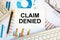 CLAIM DENIED is written in a document on the office desk